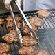 Person with tongs flipping burgers on grill